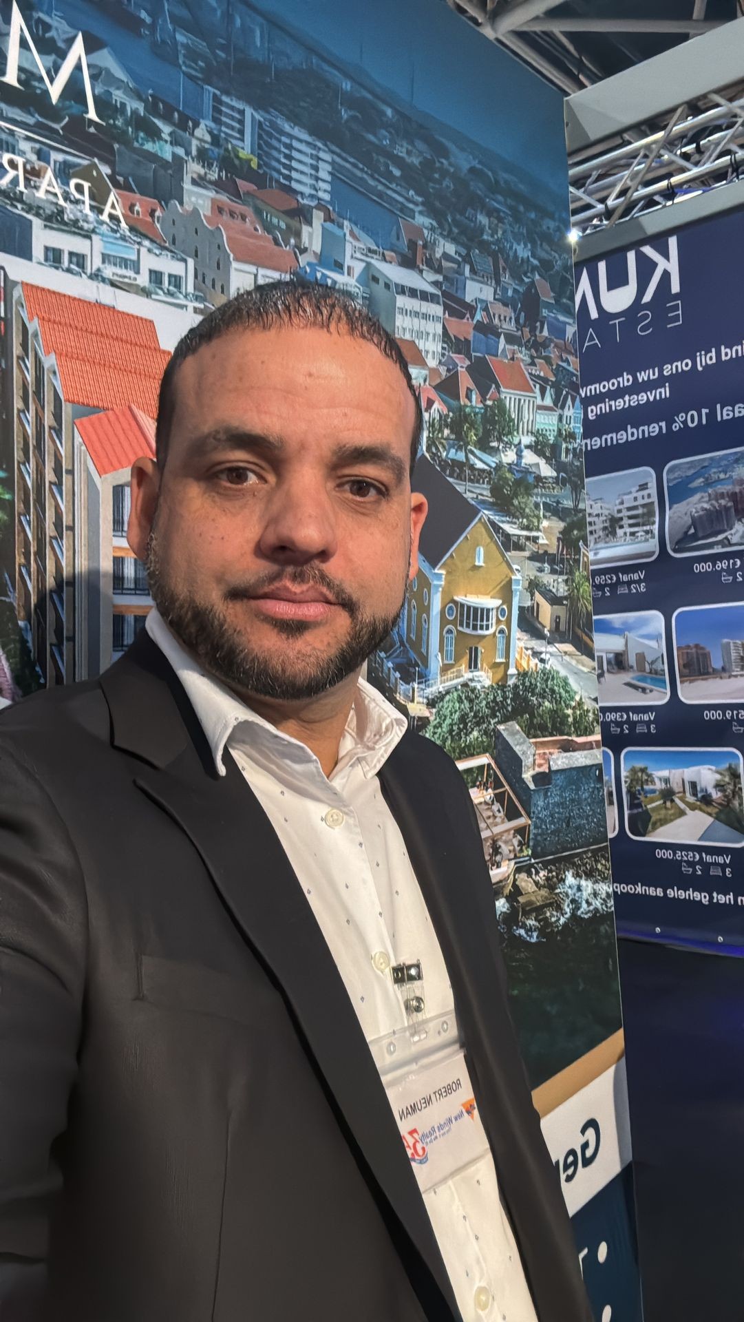 Man in a suit standing in front of a display with images and text about real estate properties.