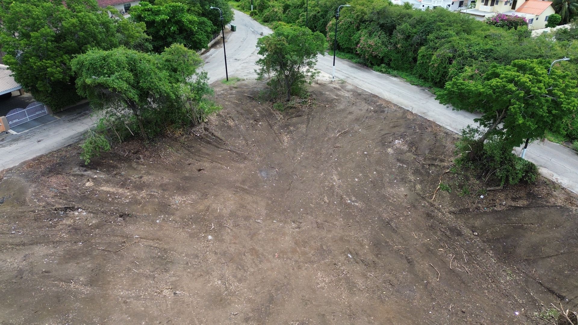 Aerial view of a large, barren plot of land surrounded by trees and residential streets.